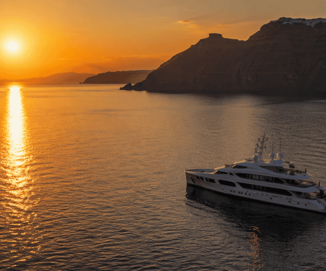 Luxury yacht cruising at sunset in Santorini with scenic caldera views.