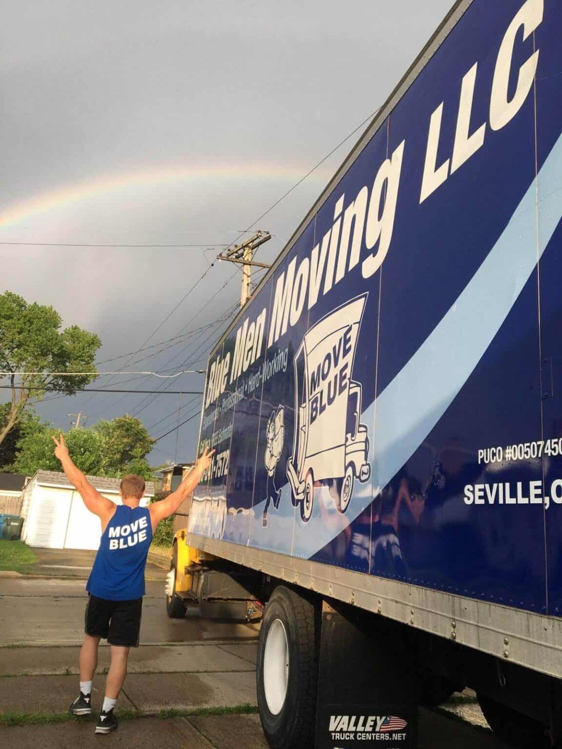 Moving Blue LLC truck with a rainbow in the sky during daytime.
