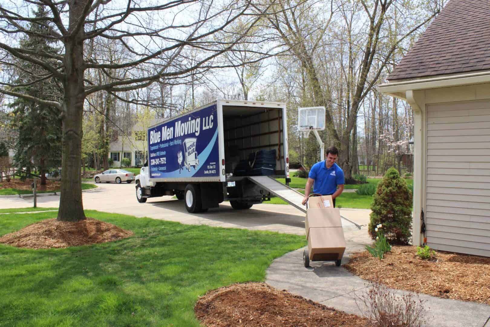 A mover unloads a storage unit into a house with a truck parked nearby in a suburban neighborhood.