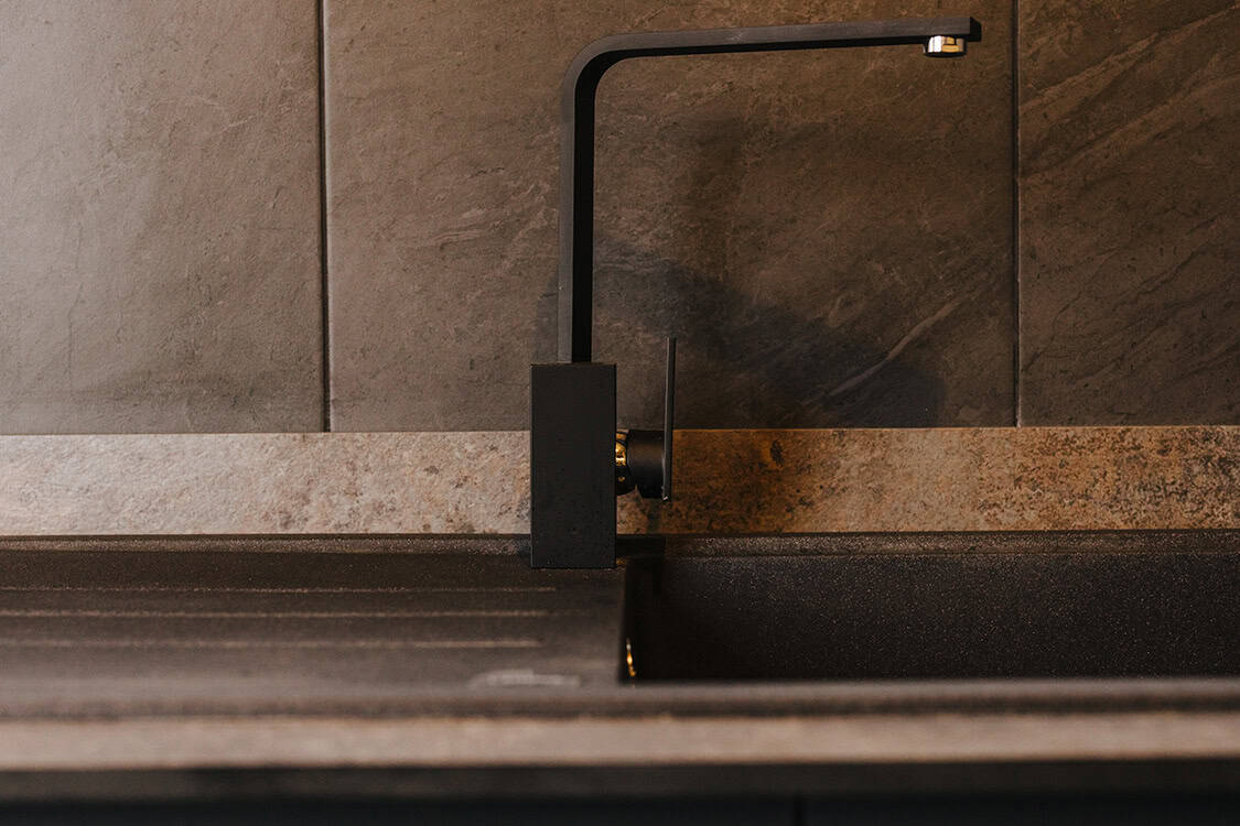 Futuristic black kitchen tap on granite countertop, modern minimalist kitchen design, eco-friendly off-grid lifestyle, sleek black kitchen sink, sustainable living, contemporary kitchen appliances, off grid home essentials.