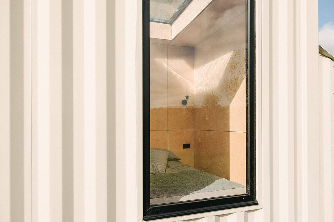 Modern off grid tiny house with large window showcasing a cozy bedroom inside for sustainable living and off-grid lifestyle experiences.