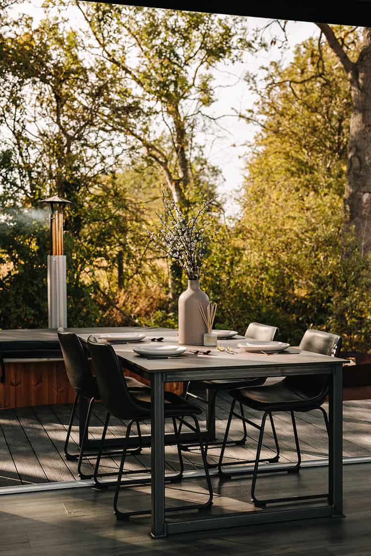 Remote outdoor dining table set on a deck overlooking lush greenery, perfect for enjoying off-grid living and sustainable outdoor living experiences.
