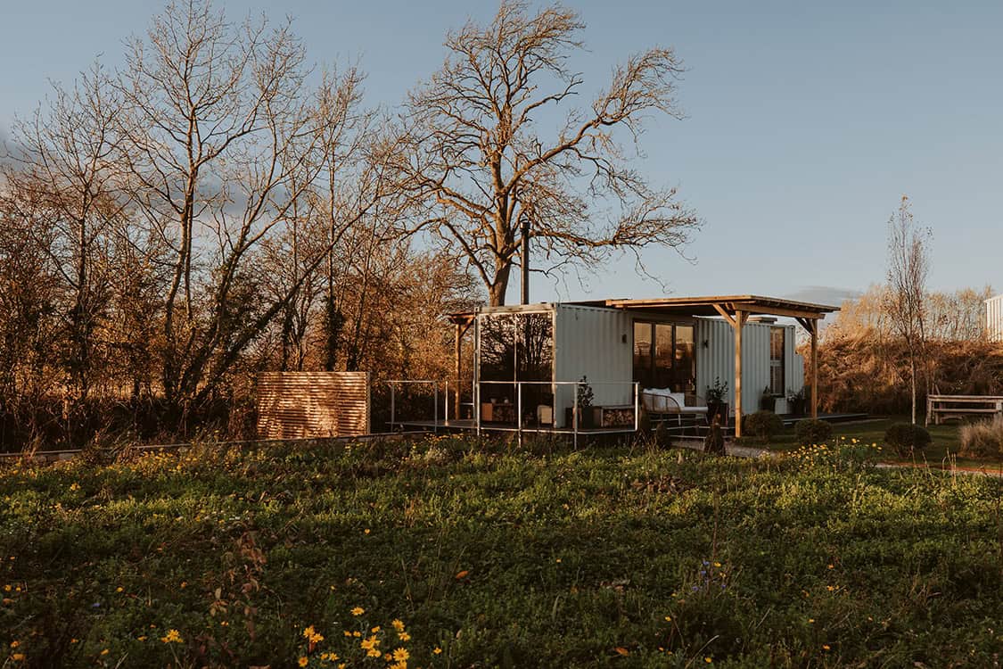 Sustainable off grid tiny house with solar power and eco-friendly design nestled in the countryside during sunset.