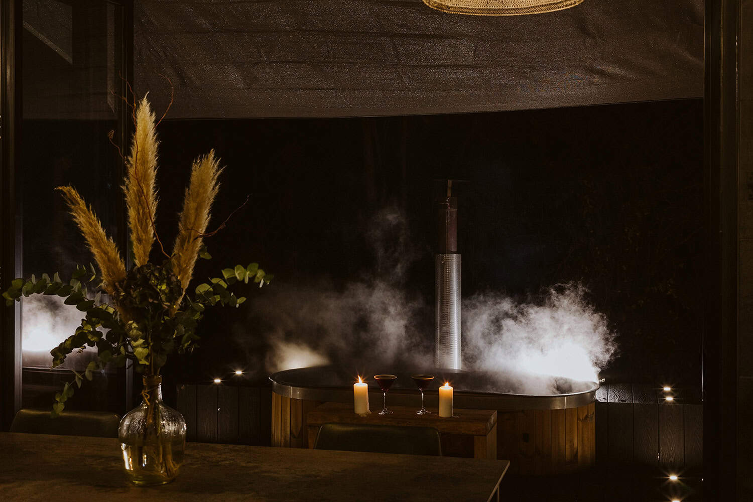 Cozy outdoor hot tub with steam rising, surrounded by candles and ambient lighting, perfect for off-grid relaxation and eco-friendly living experiences in a nature-inspired setting.