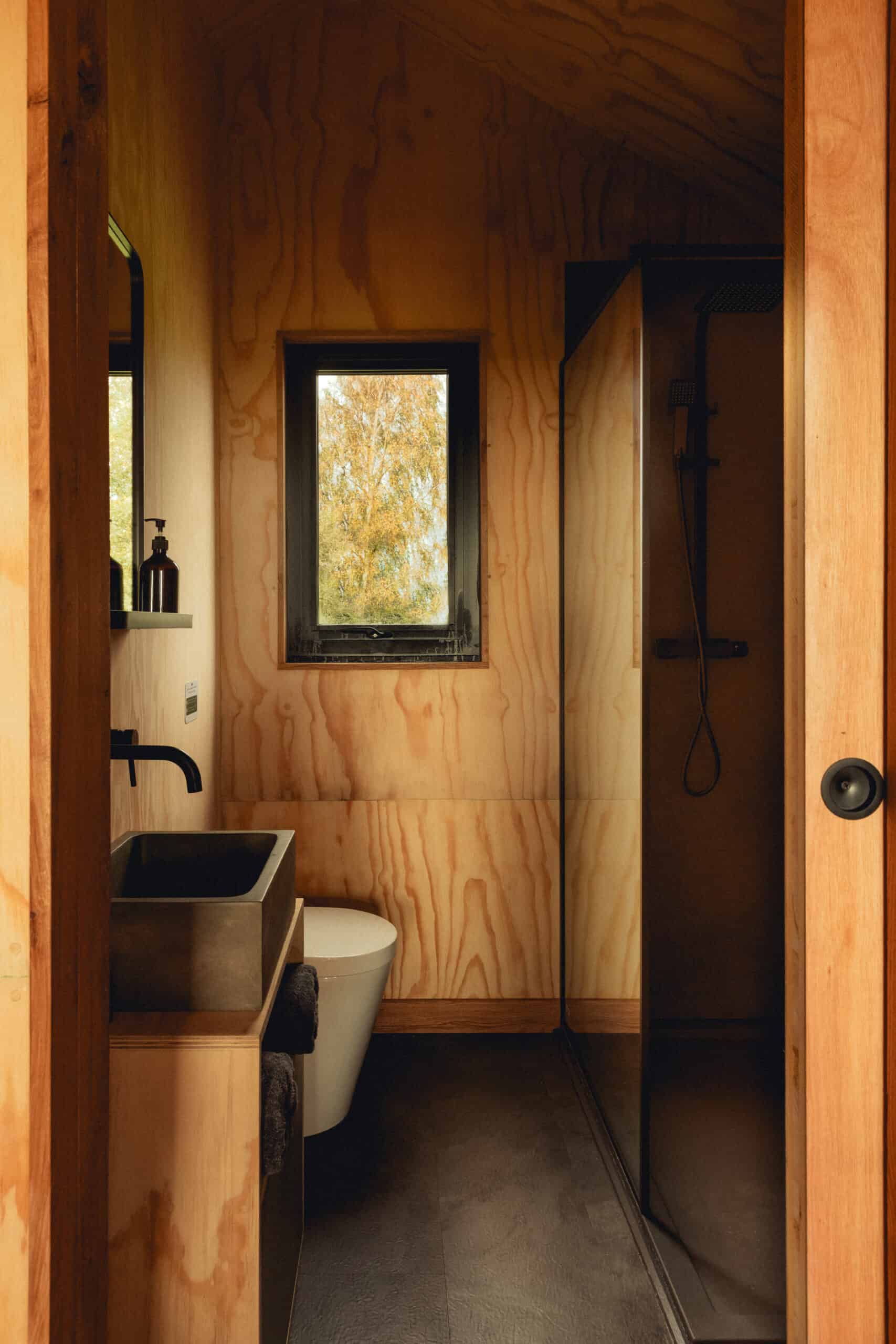 Eco-friendly off-grid bathroom with wooden interior, compact shower, and natural lighting, perfect for sustainable living in off-grid cabins.