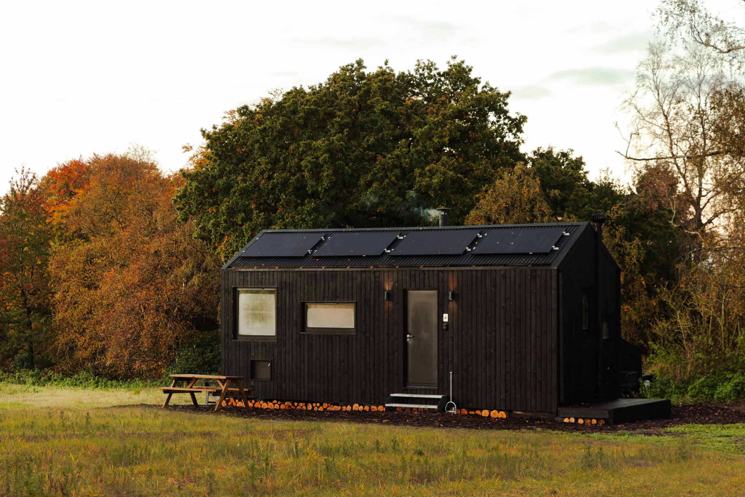 Eco-friendly off grid tiny house with solar panels on the roof amidst a nature setting. Sustainable living in a black wooden cabin, perfect for off grid experiences.