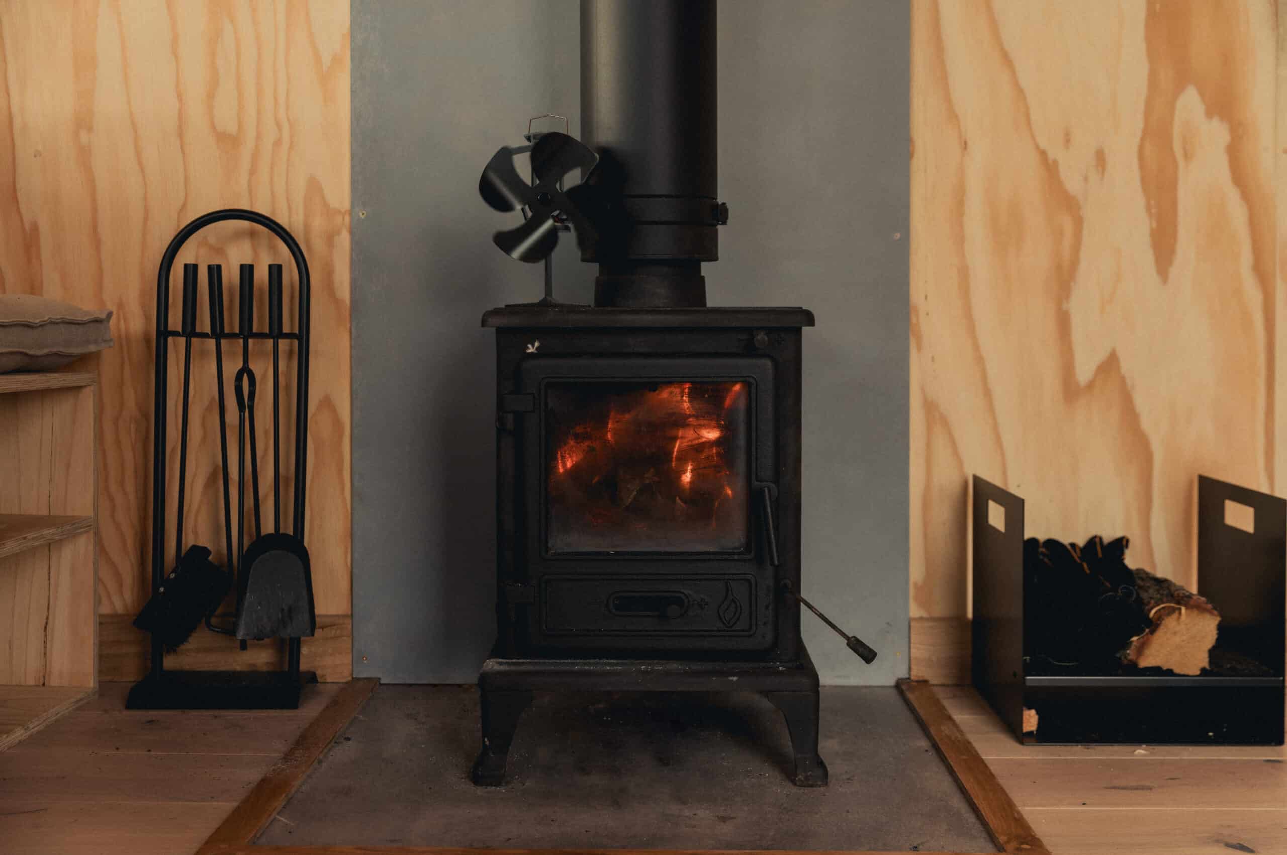 Wood burning stove with fire in a tiny off grid cabin living space, eco-friendly heating for remote off grid living, sustainable off grid lifestyle.