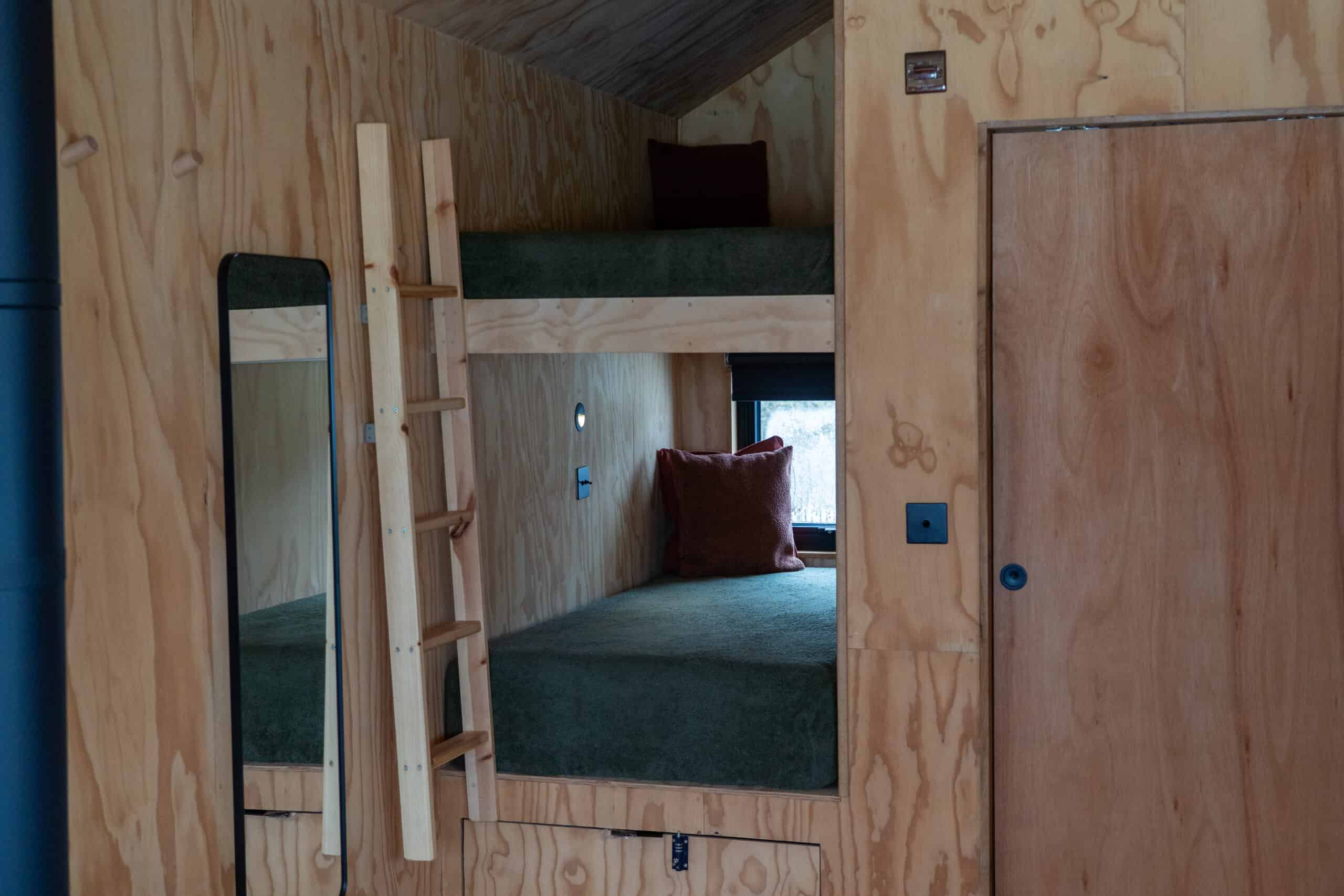 Cozy wooden interior with built-in bunk beds and small window, showcasing off-grid living accommodation, eco-friendly cabin, minimalistic interior design, perfect for eco-conscious lifestyles.