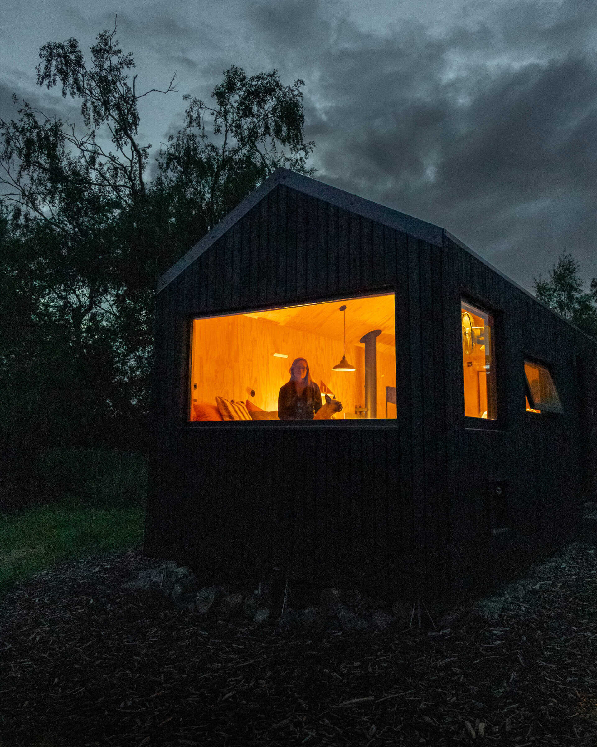 Cozy off-grid tiny house at night with warm interior lighting, surrounded by nature, ideal for sustainable living and off grid holidays.