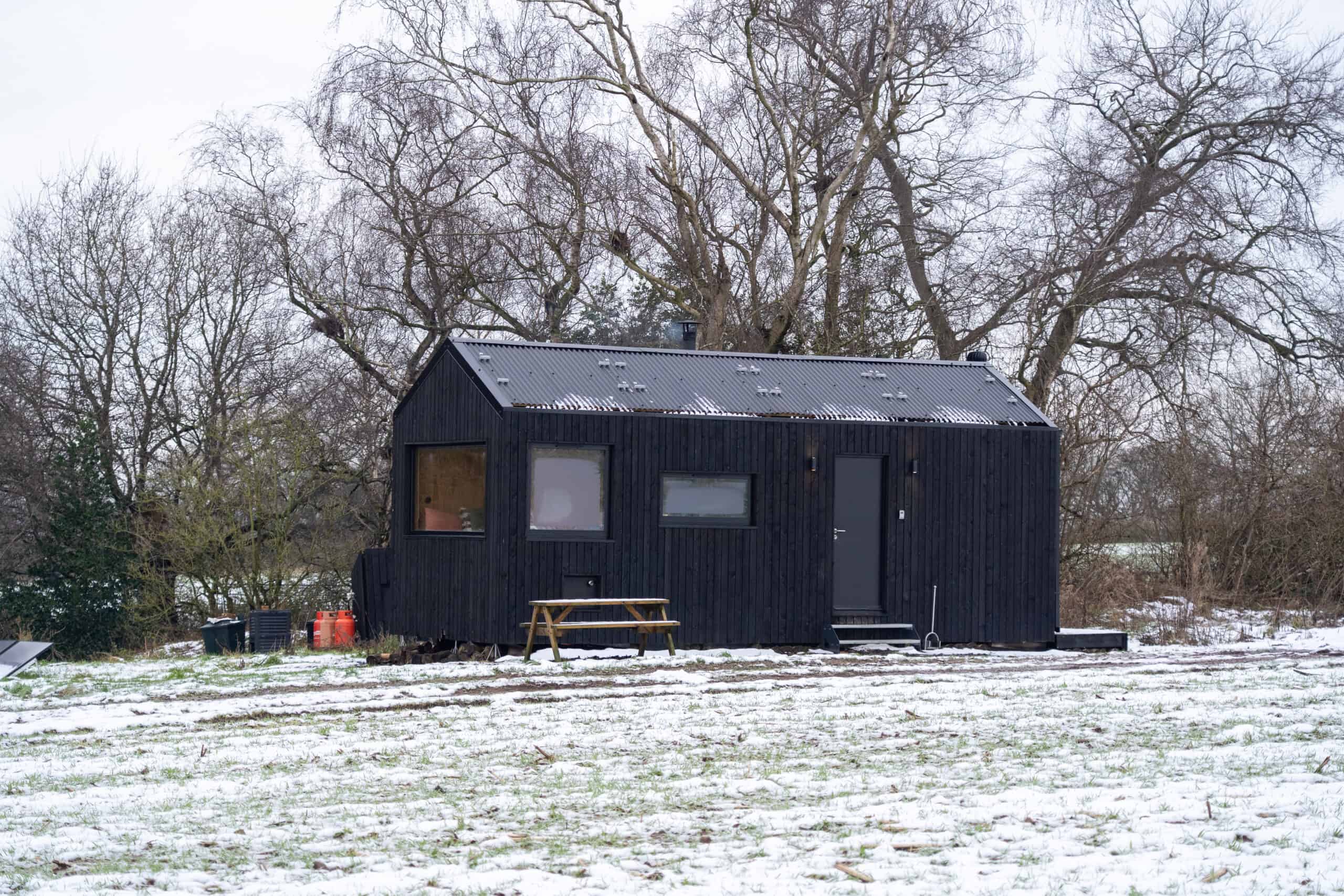 Cozy off-grid tiny house in winter natural setting, eco-friendly sustainable living, modern black wooden cabin, off-grid shelter for ultimate independence, ideal for sustainable off grid lifestyle.