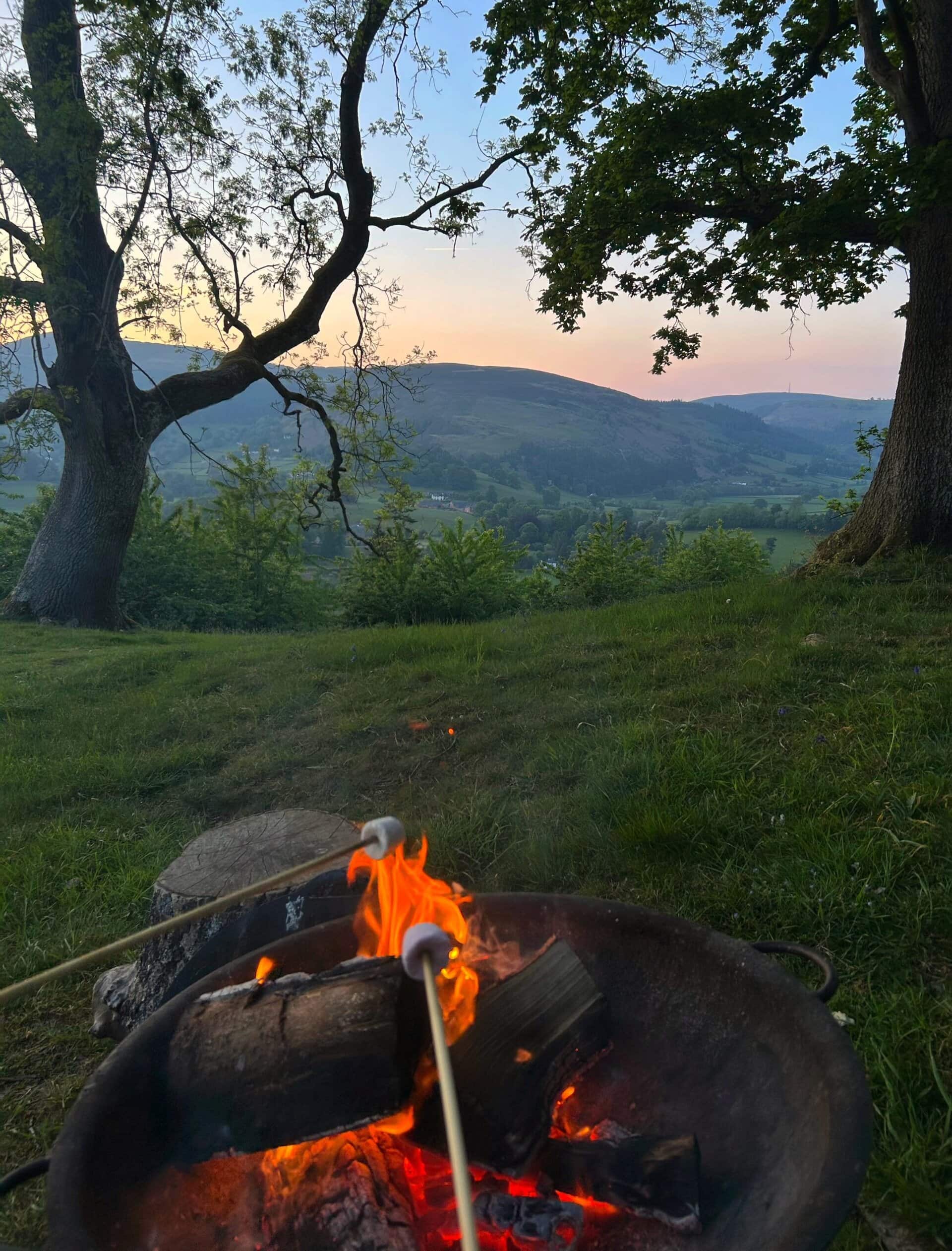 A peaceful off-grid camping scene with a campfire, lush trees, and rolling hills at dusk, perfect for sustainable living and off-grid adventures.