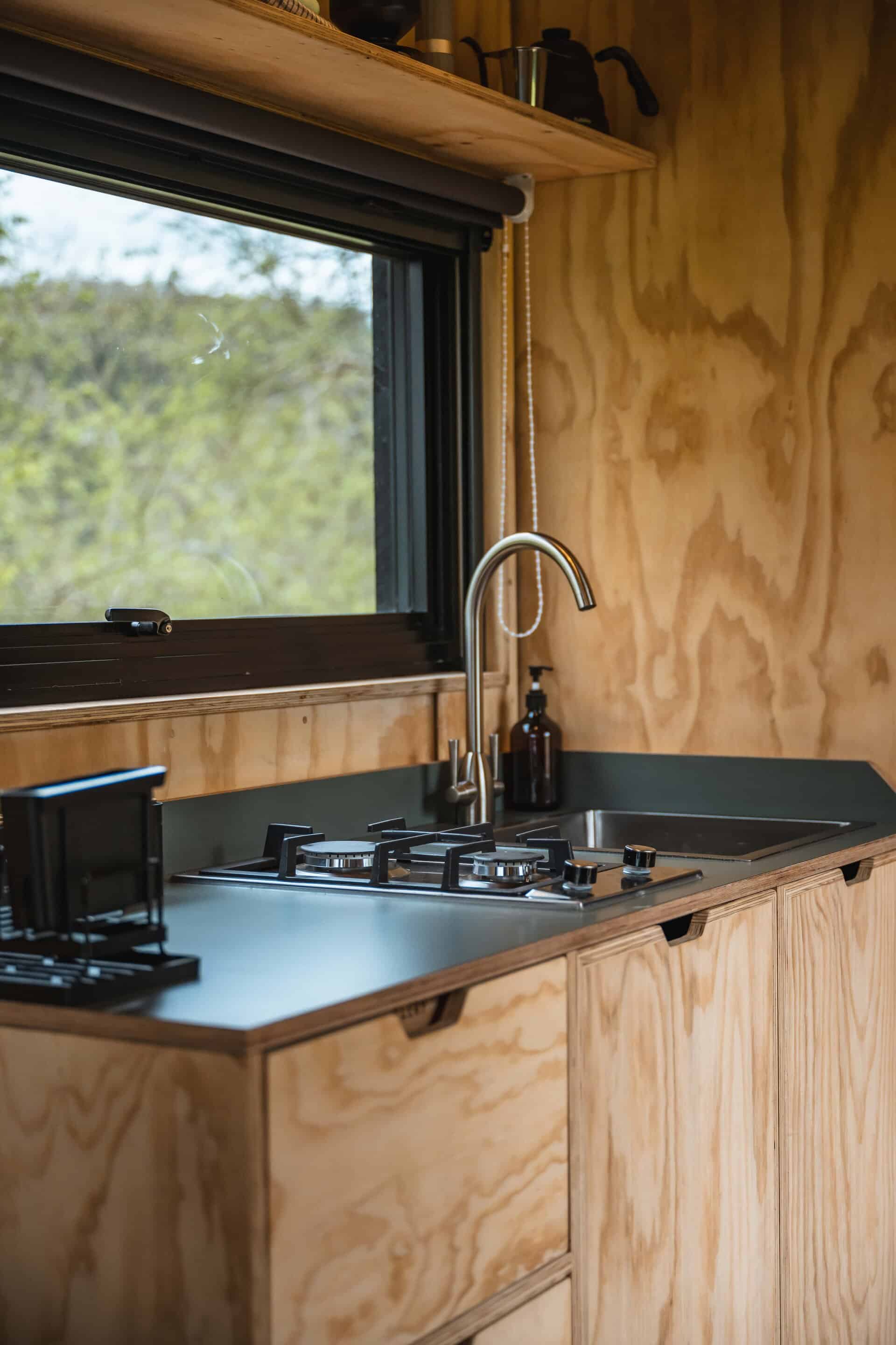 Eco-friendly off grid kitchen with wooden cabinetry and a modern gas stove, large window showing green nature, showcasing sustainable living and self-sufficient off grid lifestyle in the UK.