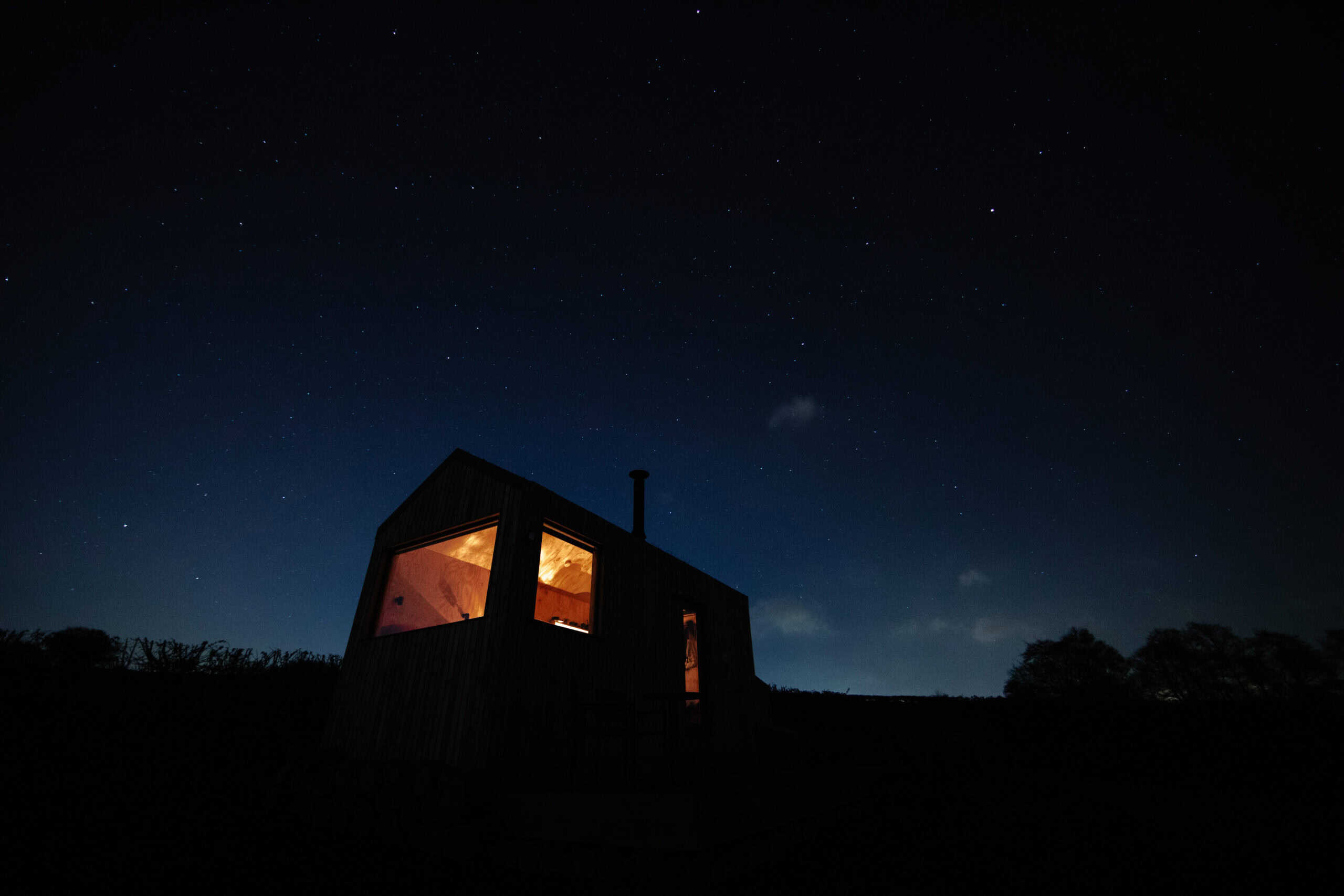 Secluded off-grid eco cabin under a starry night sky with illuminated windows, perfect for sustainable outdoor holidays and eco-friendly escapes.