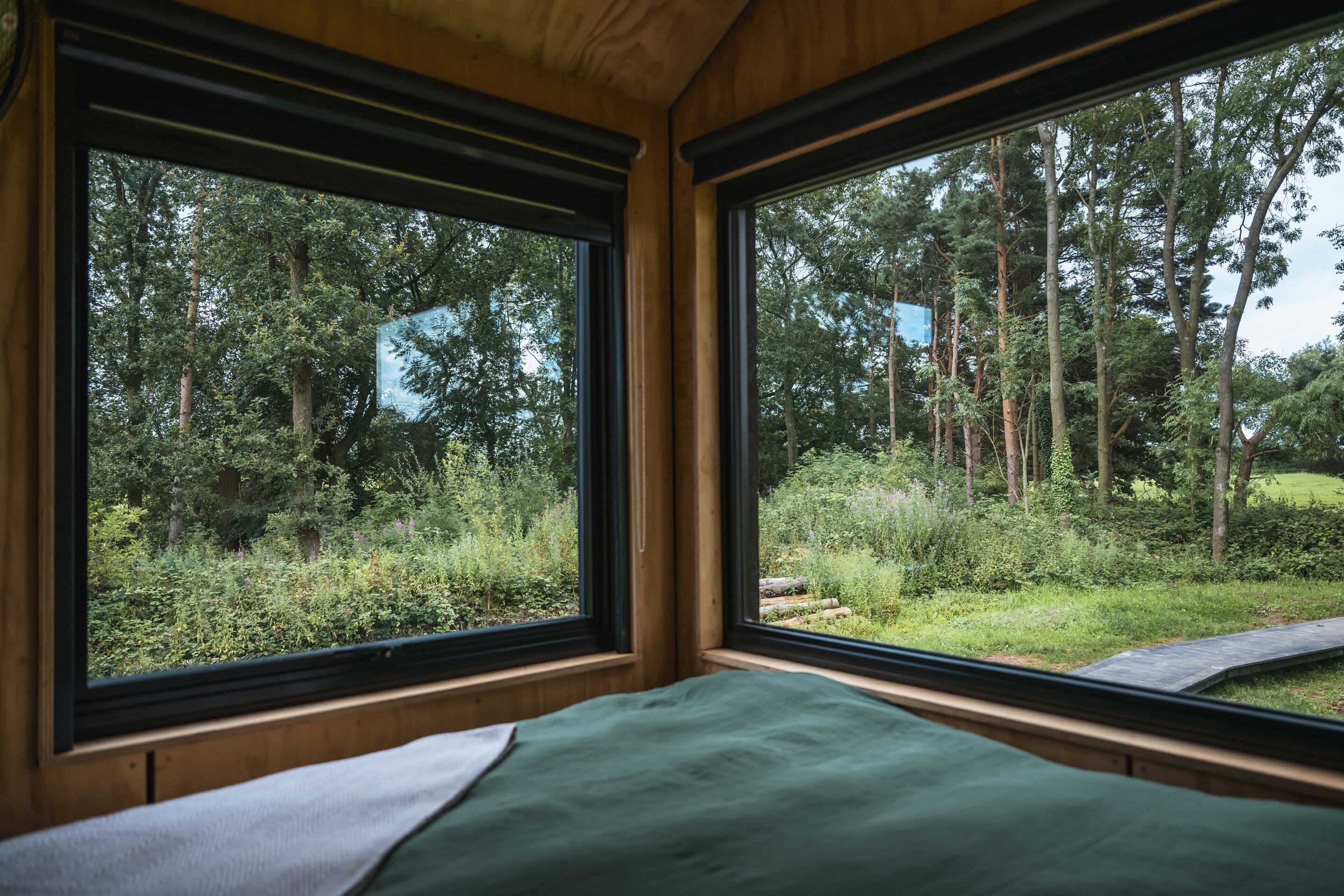Secluded off-grid wooden cabin with large windows showcasing a lush green forest and natural eco-friendly surroundings, perfect for sustainable living and nature retreats.