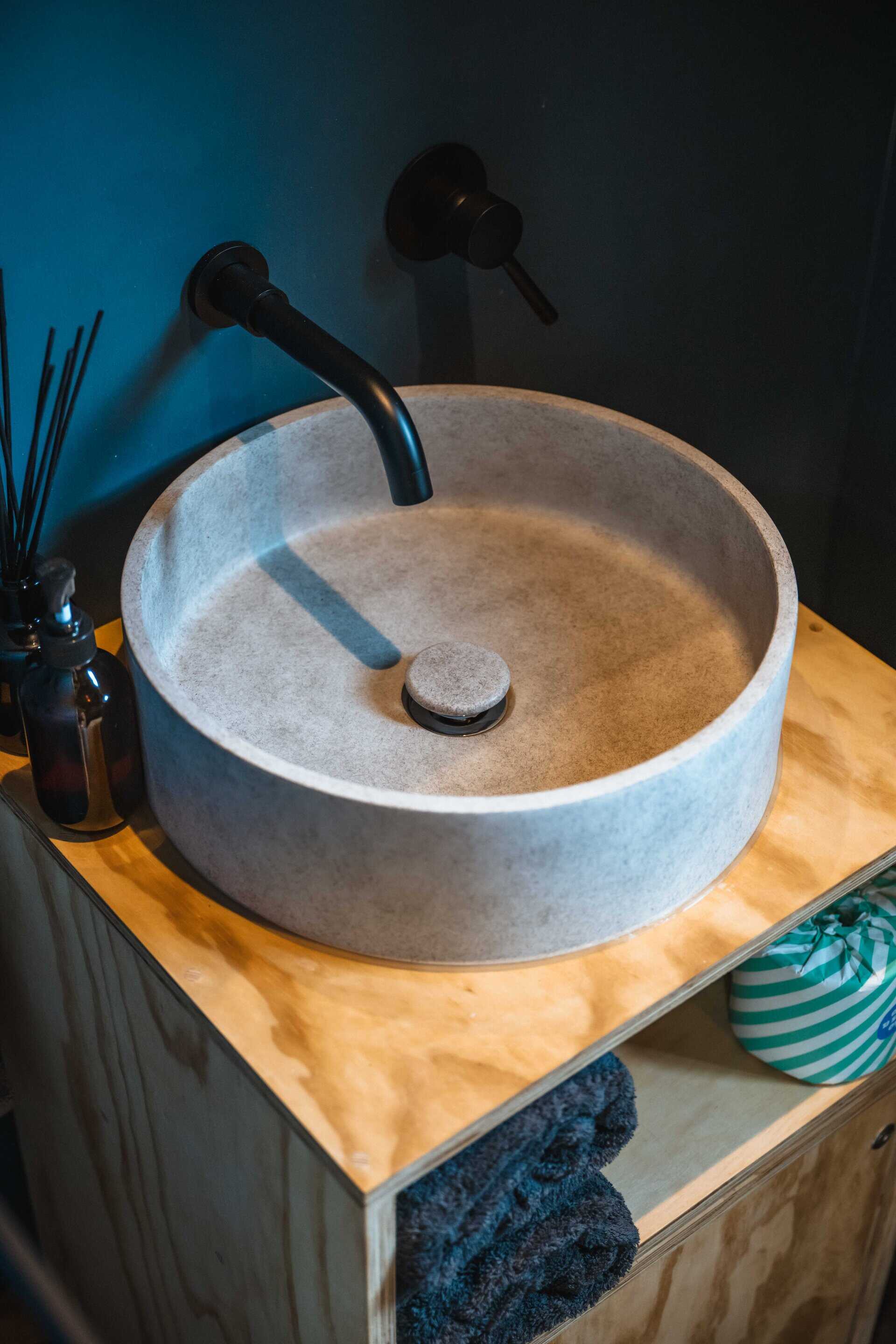 Black matte wall-mounted faucet over a modern, round stone sink in an off-grid tiny home bathroom. Sustainable living, off-grid lifestyle, tiny house bathroom, eco-friendly design, minimalist off-grid cabin.