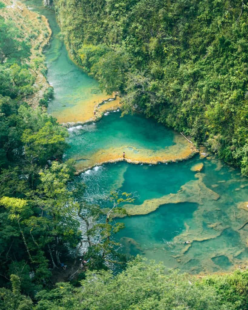The stunning view of Semuc Champey from above with a lone traveler stood in the middle of the terraced pools