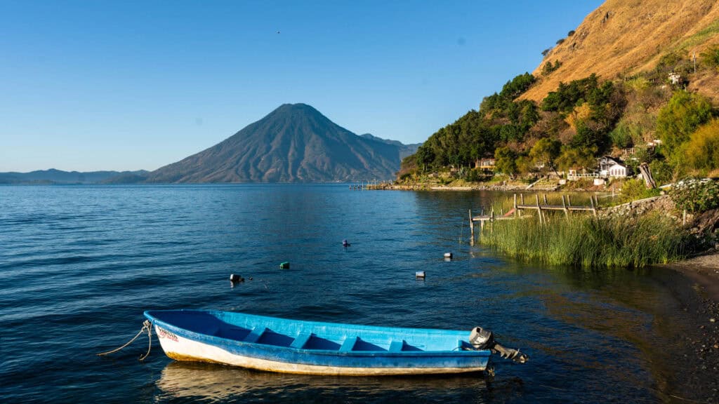 A lone canoe floating on Lake Atitlan with towering volcanoes in the background