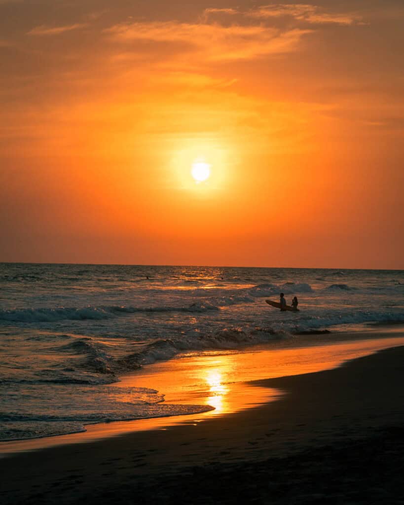 A couple of surfers walking out into the ocean for a sunset surf in El paredon, guatemala