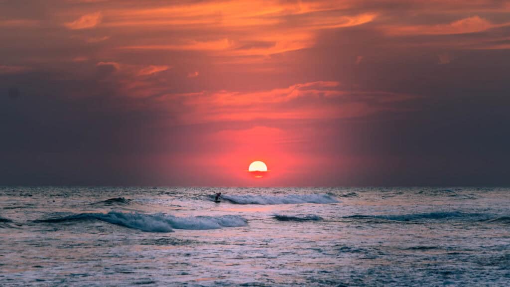 A lone surfer riding a wave infant of an incredible sunset in El paredon, Guatemala