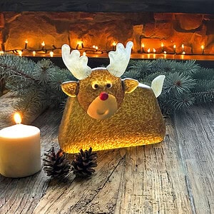 Rentier-Skulptur RUDOLF auf einem winterlich dekorierten Holztisch mit Kerze
