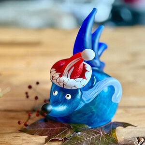 Blue Christmas hedgehog SANTA SPIKE with a red Santa hat on a wooden table decorated with leaves and red berries.
