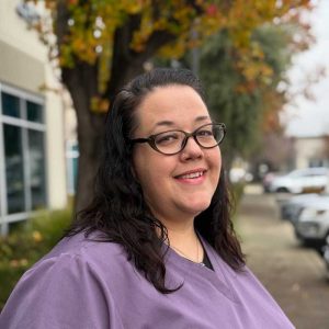 Confident woman in purple scrubs outdoors.