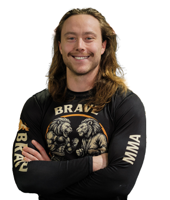 Adam Marsh with long hair, wearing a black MMA-themed shirt, standing in a fitness environment.