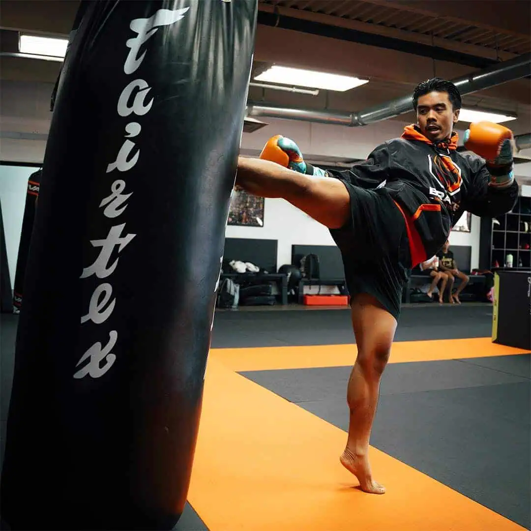Powerful martial arts athlete delivering a high kick to the punching bag at Bravé MMA and Fitness.