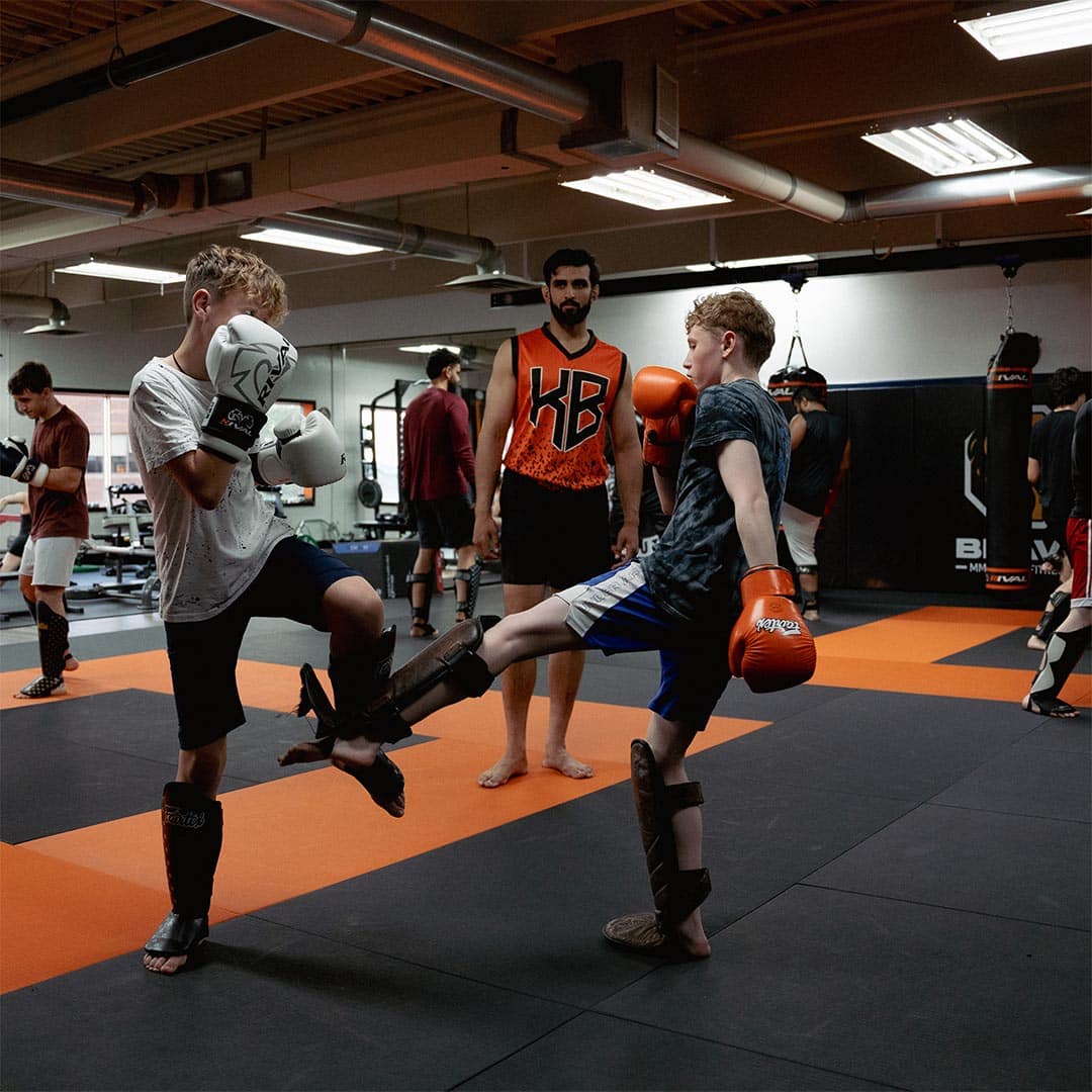 Kids martial arts training at Bravé MMA and Fitness with sparring and protective gear in a professional gym setting.