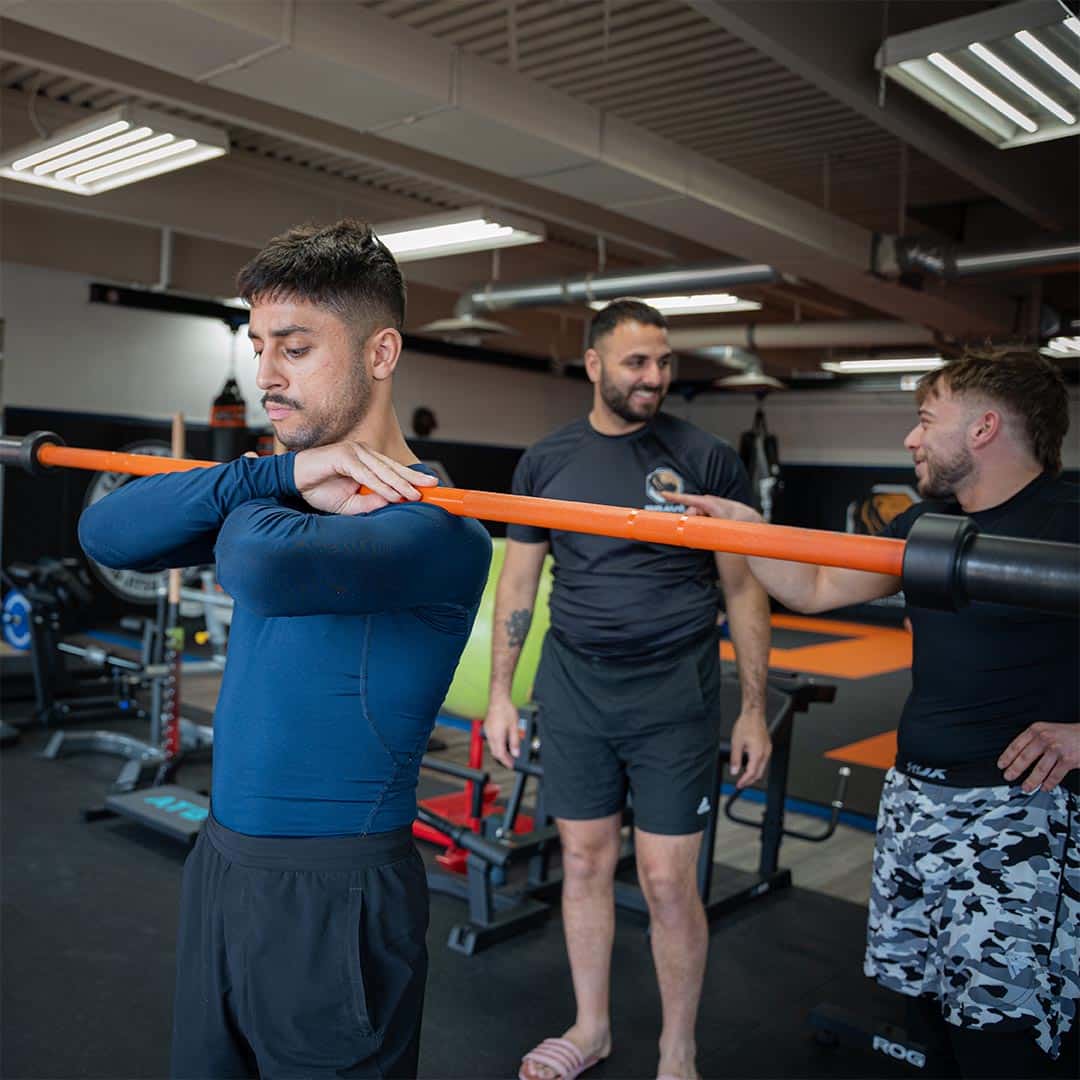 Young man performing a shoulder stretch with a barbell at Bravé MMA and Fitness gym.