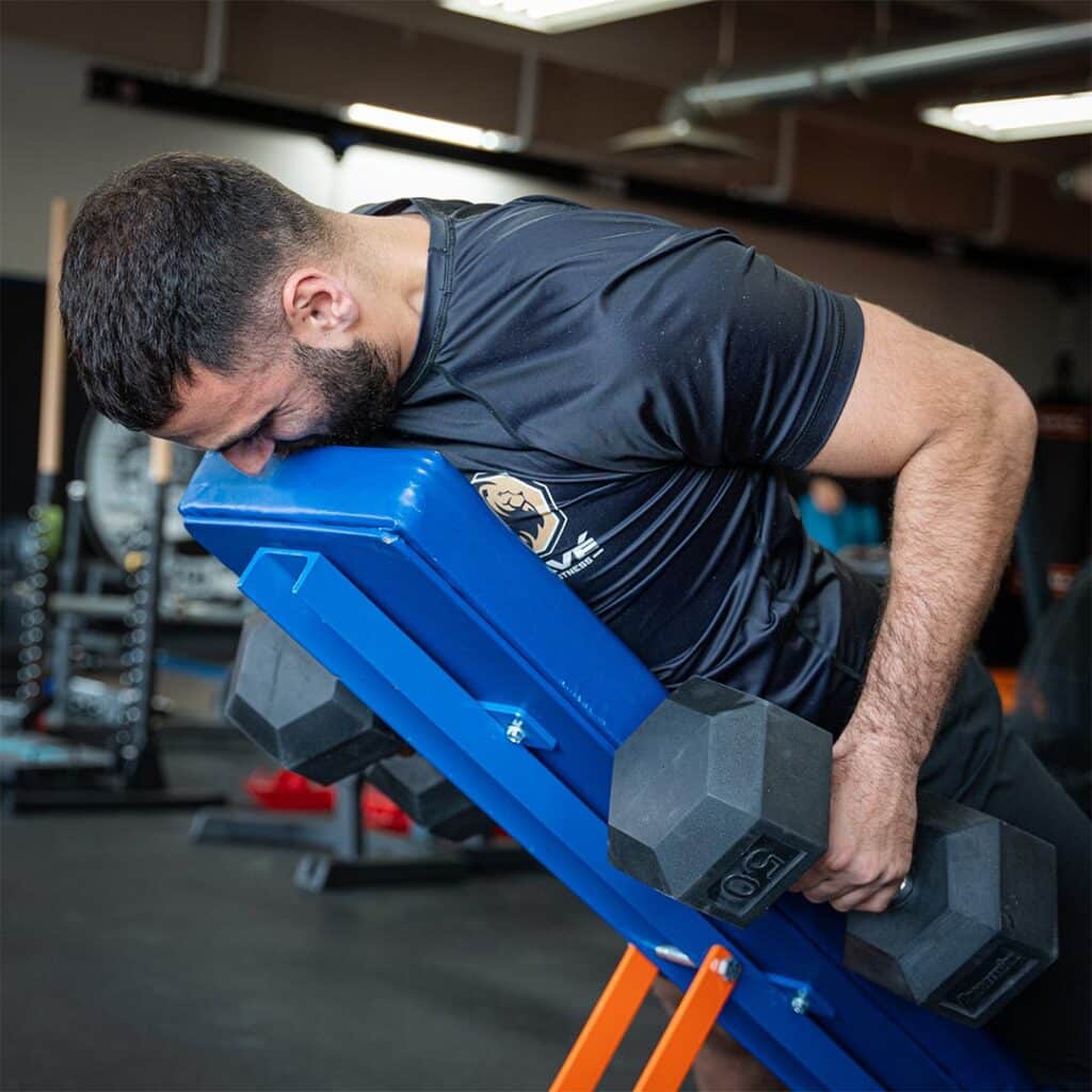 Heavyweight man performing incline dumbbell press for strength training at Bravé MMA And Fitness.