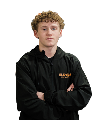 Young male athlete Noah Kelleher standing confidently with arms crossed, wearing a black jacket with "BRAY" logo, in an indoor sports facility.