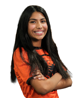Portrait of Mia Sethi smiling confidently, wearing an orange sports jersey, with long dark hair and a friendly expression, standing against a blurred background.