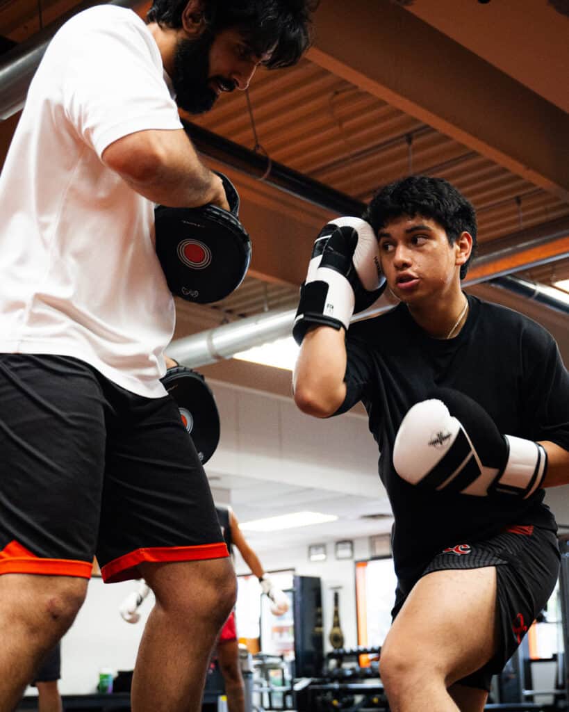 Young male boxer practicing punches with coach in gym during free trial class, focusing on technique and fitness.