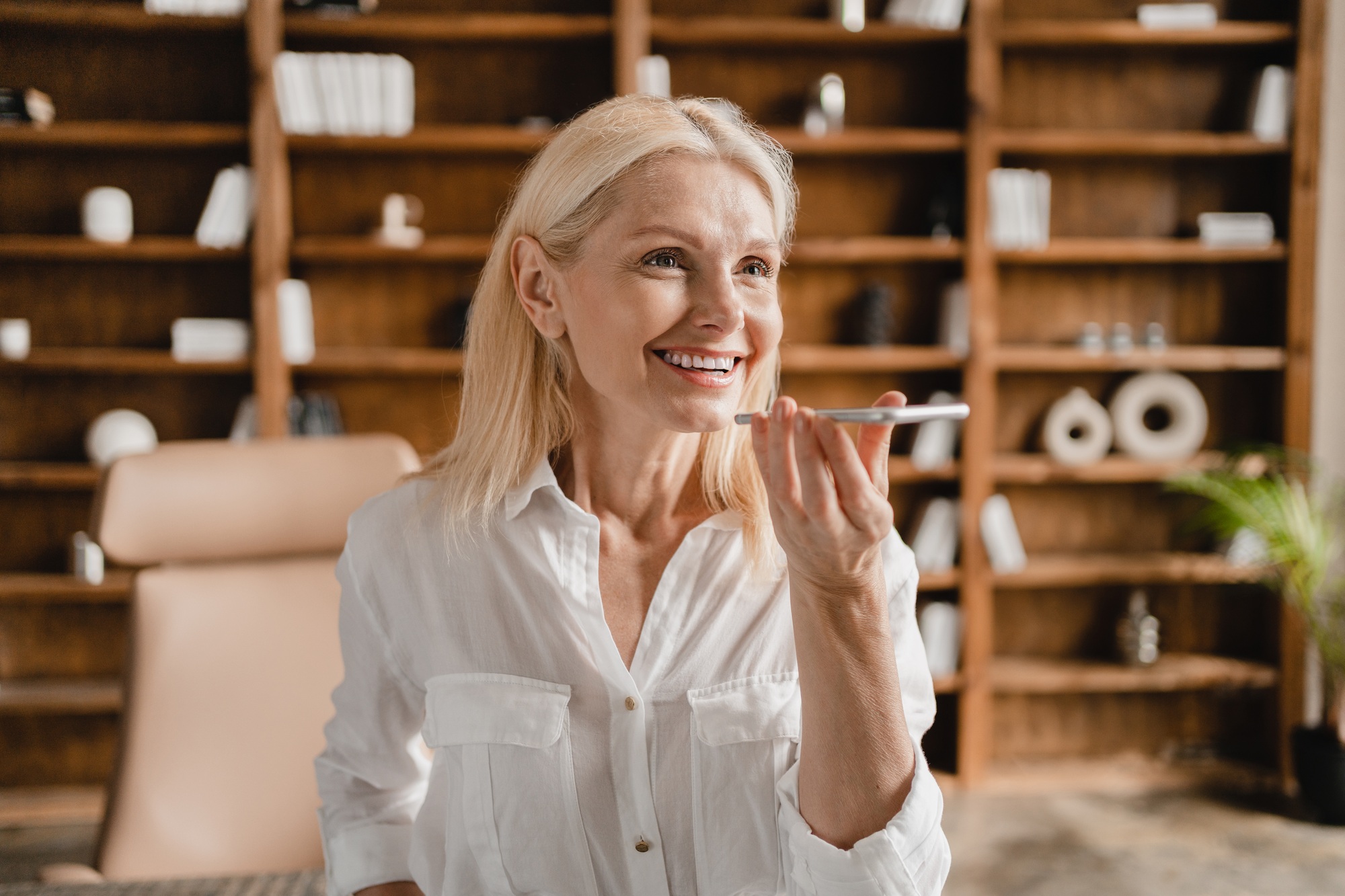 Businesswoman recording voice message on cellphone while working remotely in office , communicating