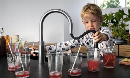 Bright young boy filling glasses with red fruit drinks in modern kitchen, showcasing custom-designed Broadoak Kitchens Ltd kitchen cabinetry and countertop for stylish home interiors.