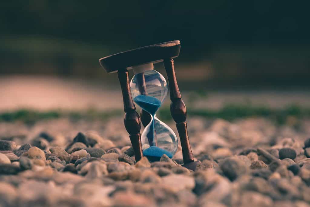 An hourglass with blue sand on a pebble beach represents effective time management and productivity tools for business success.