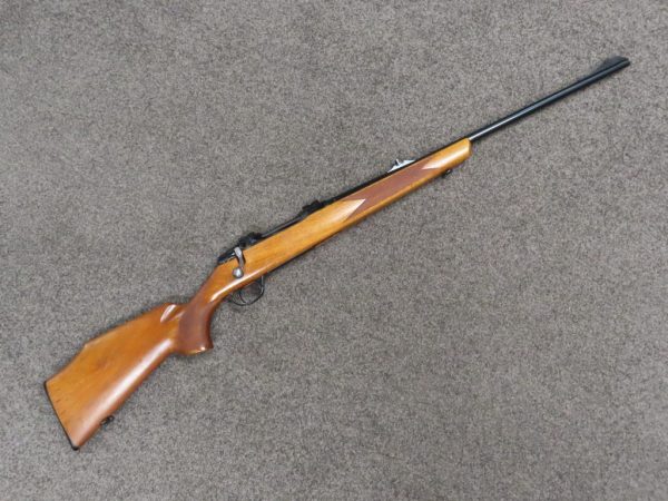 A vintage bolt-action rifle with wooden stock on a grey surface. Perfect for firearm collectors and shooting enthusiasts.