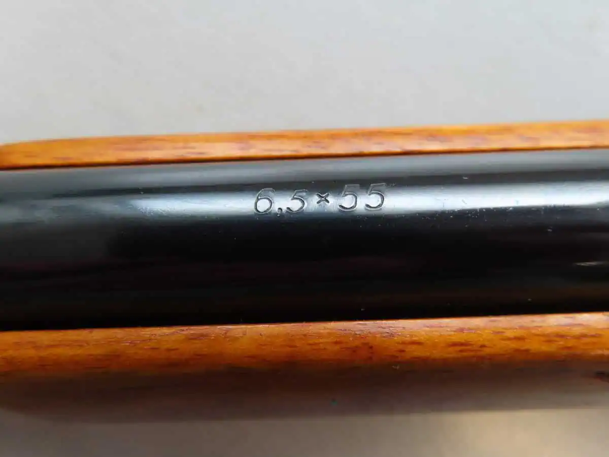 A close-up of a firearm barrel showing “6.5×55” caliber engraved, connected to NZ ammunition history.