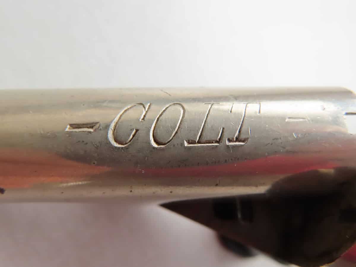 Close-up of engraved "COLT" on metal firearm part, showing historical vintage firearm branding.