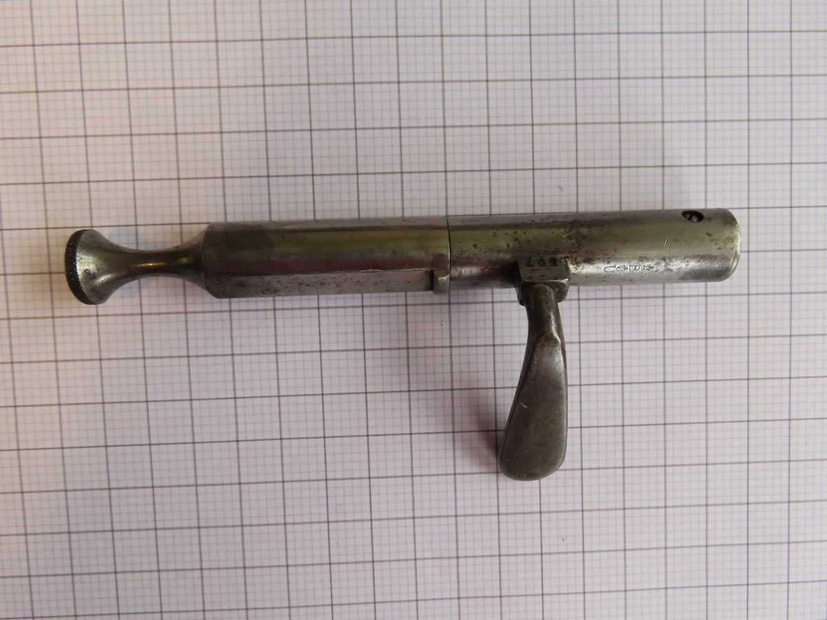 Metal firearm part with handle on grid background, representing classic ammunition tools.