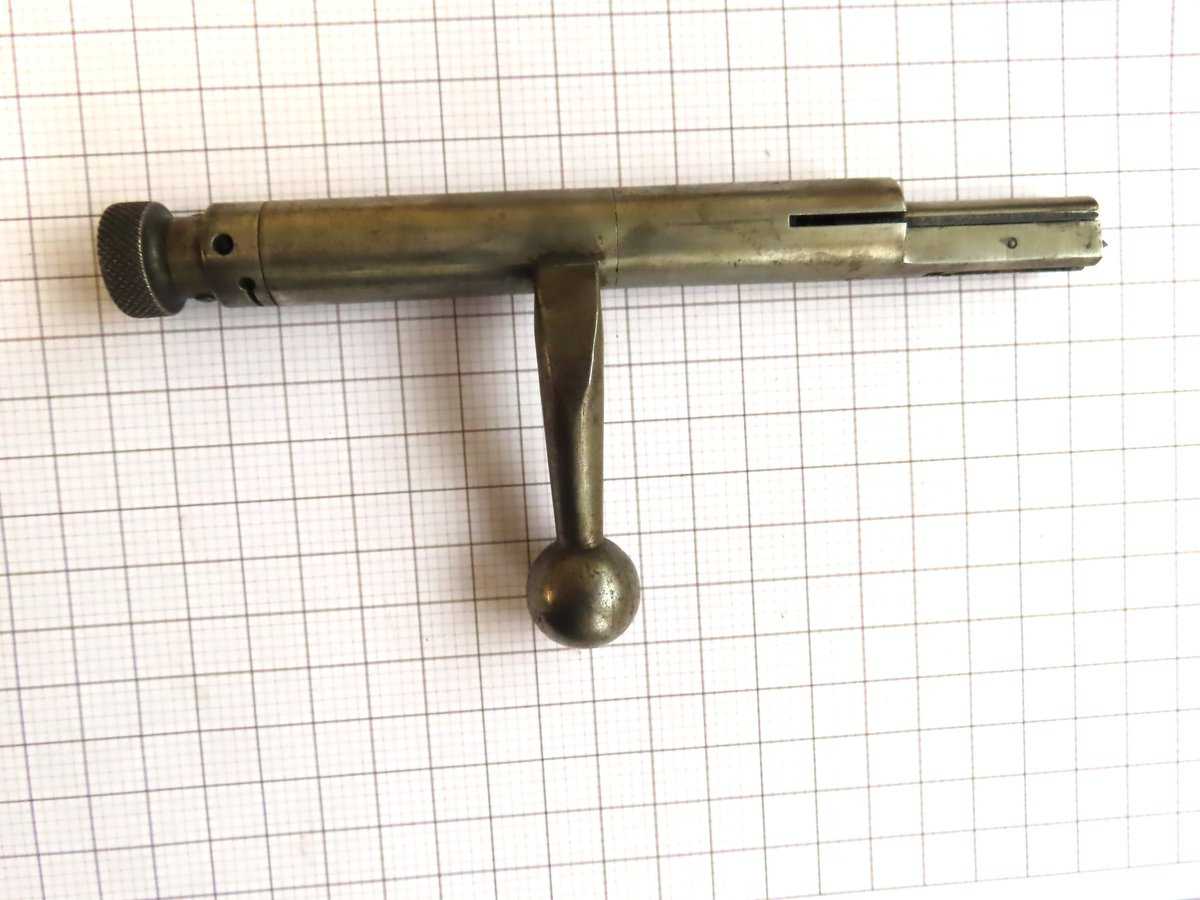 Alt text: Old silver bolt handle part for vintage firearm, placed on grid paper background.