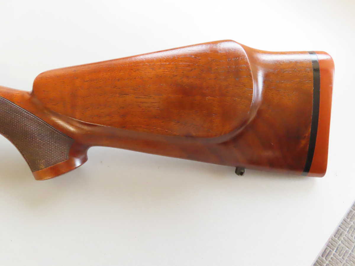 Close-up of polished wooden rifle stock with checkered grip detail.