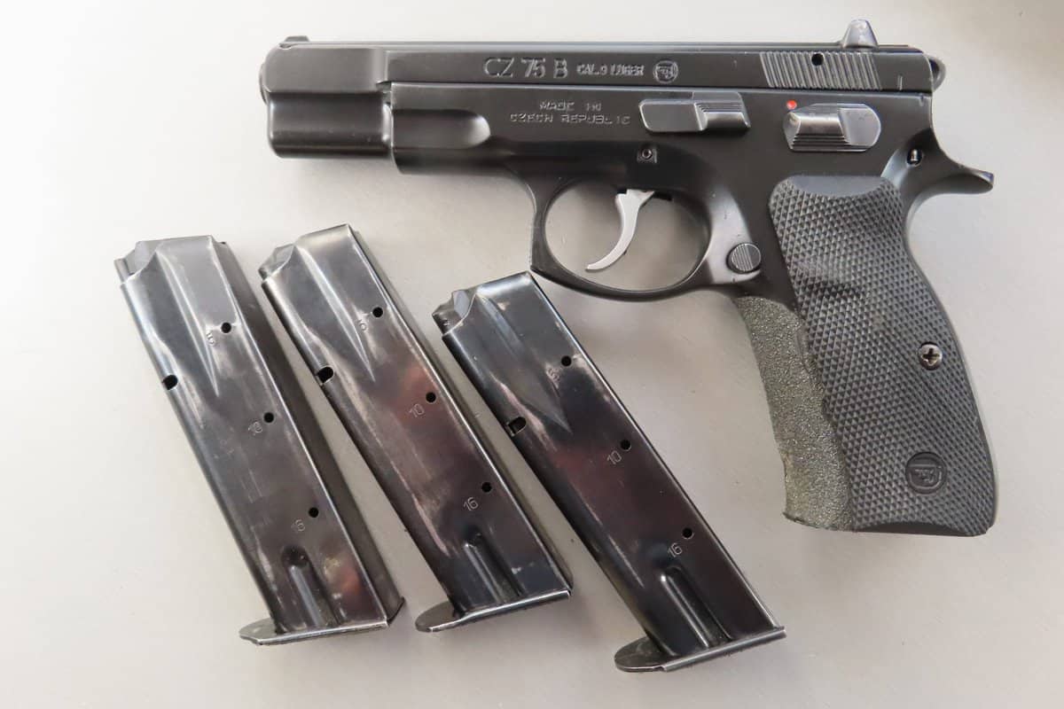 Close-up of a CZ 75 B semi-automatic pistol with three magazines on a white surface.