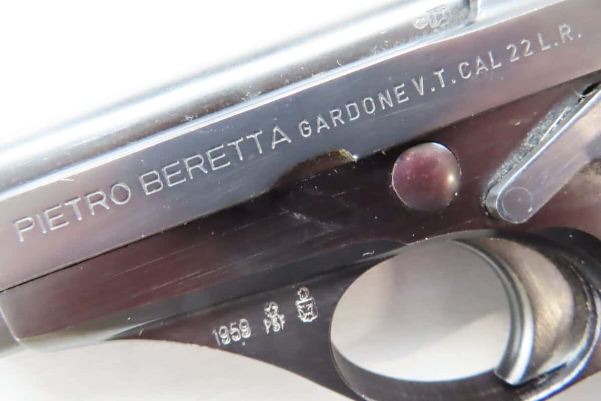 Close-up of a vintage pistol with inscriptions "PIETRO BERETTA GARDONE V.T. CAL. 22 LR" on the firearm's slide.