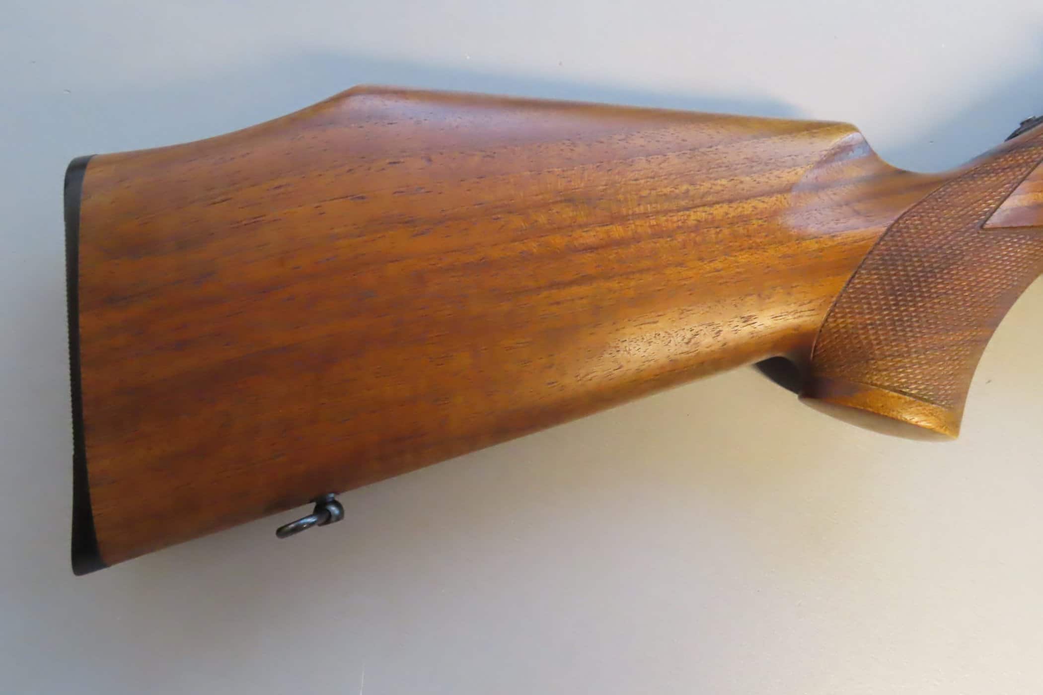 Close-up of a polished wooden rifle stock with checkered grip detail, highlighting quality gun components.
