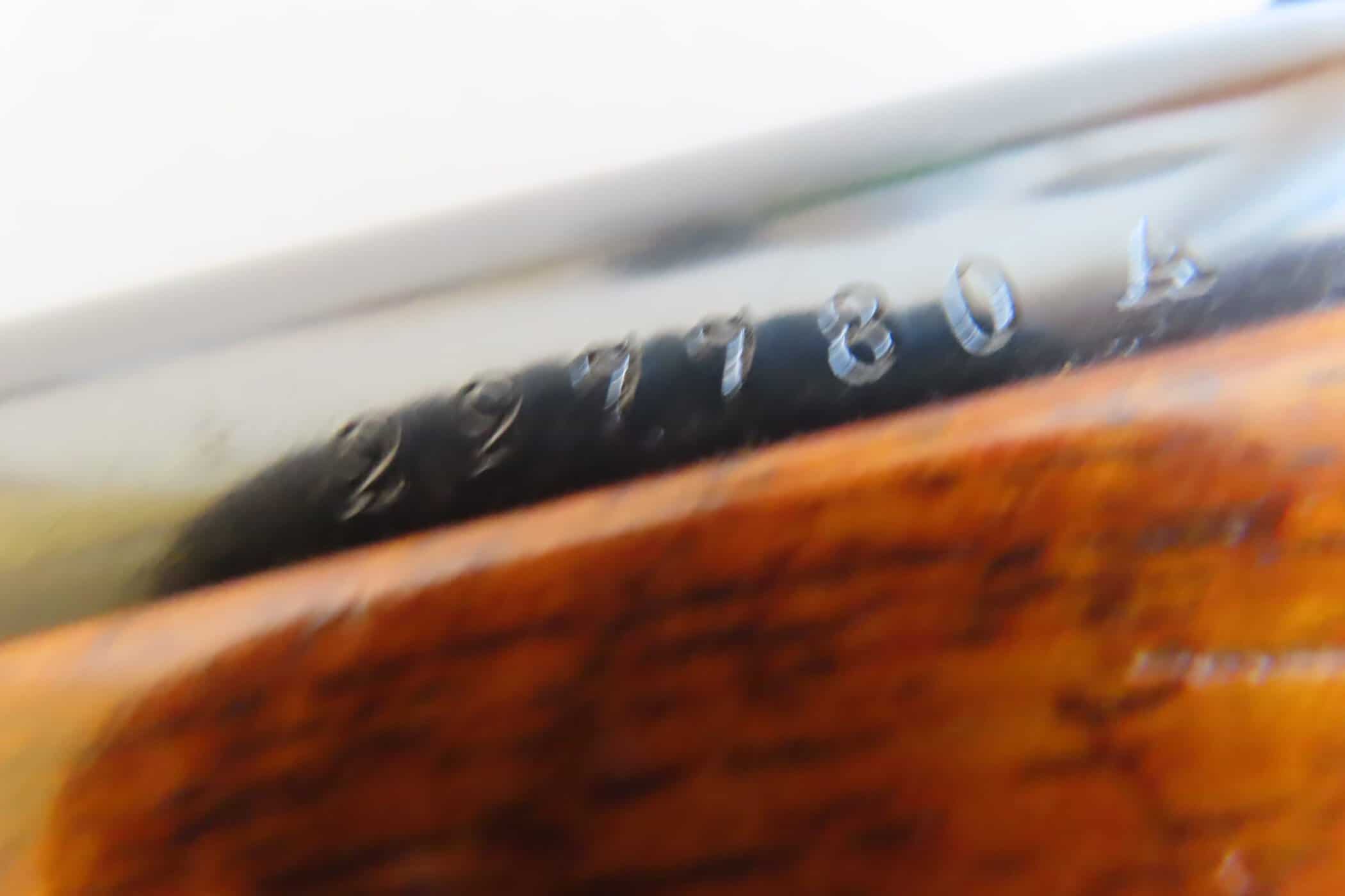 Close-up of vintage firearm serial number and markings on a wooden gun stock.