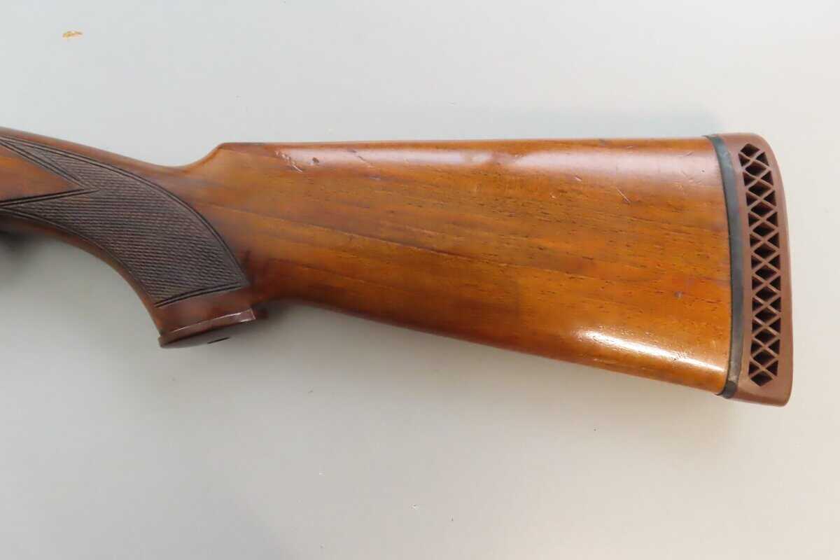 Close-up of polished wooden rifle stock with checkered grip detail.
