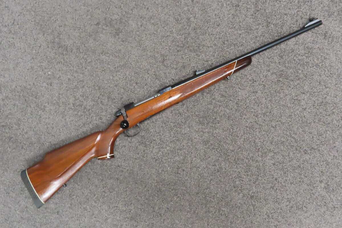 Antique rifle with wooden stock on beige carpet floor, ideal for collectors or shooting enthusiasts in New Zealand.