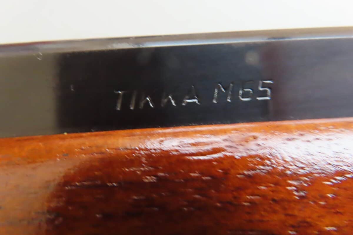 Close-up of black metal section with "TIKKA TMG 5" engraving, wooden stock below, in Classic Ammunition Company display.